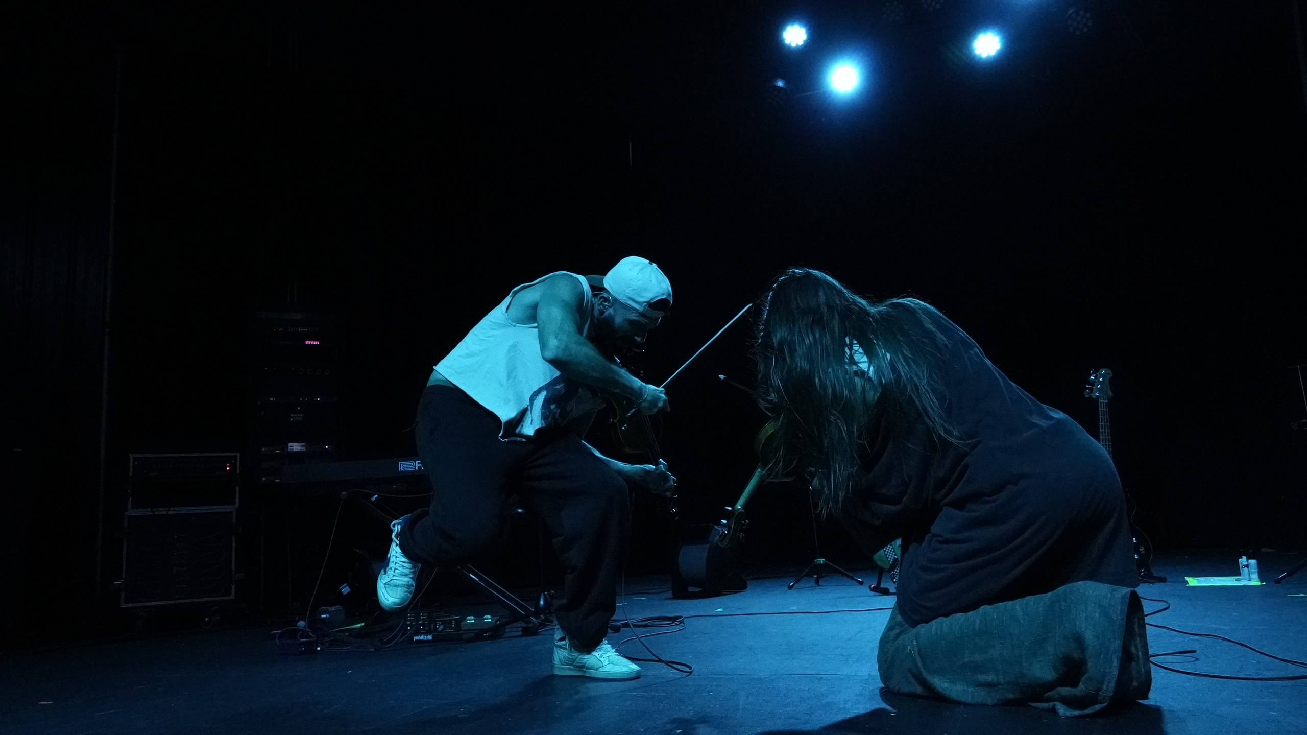 Two musicians performing face to face on a dark stage under blue spotlights