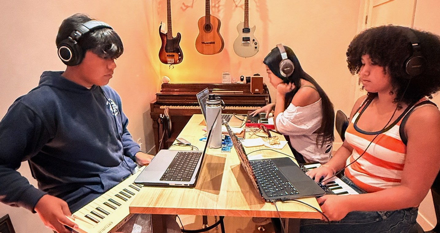 Teen students in headphones making music on laptops and keyboards in a studio